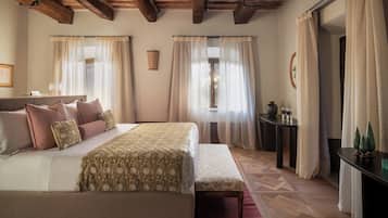 Quarto com cama grande, um banco, uma mesa pequena e cortinas.