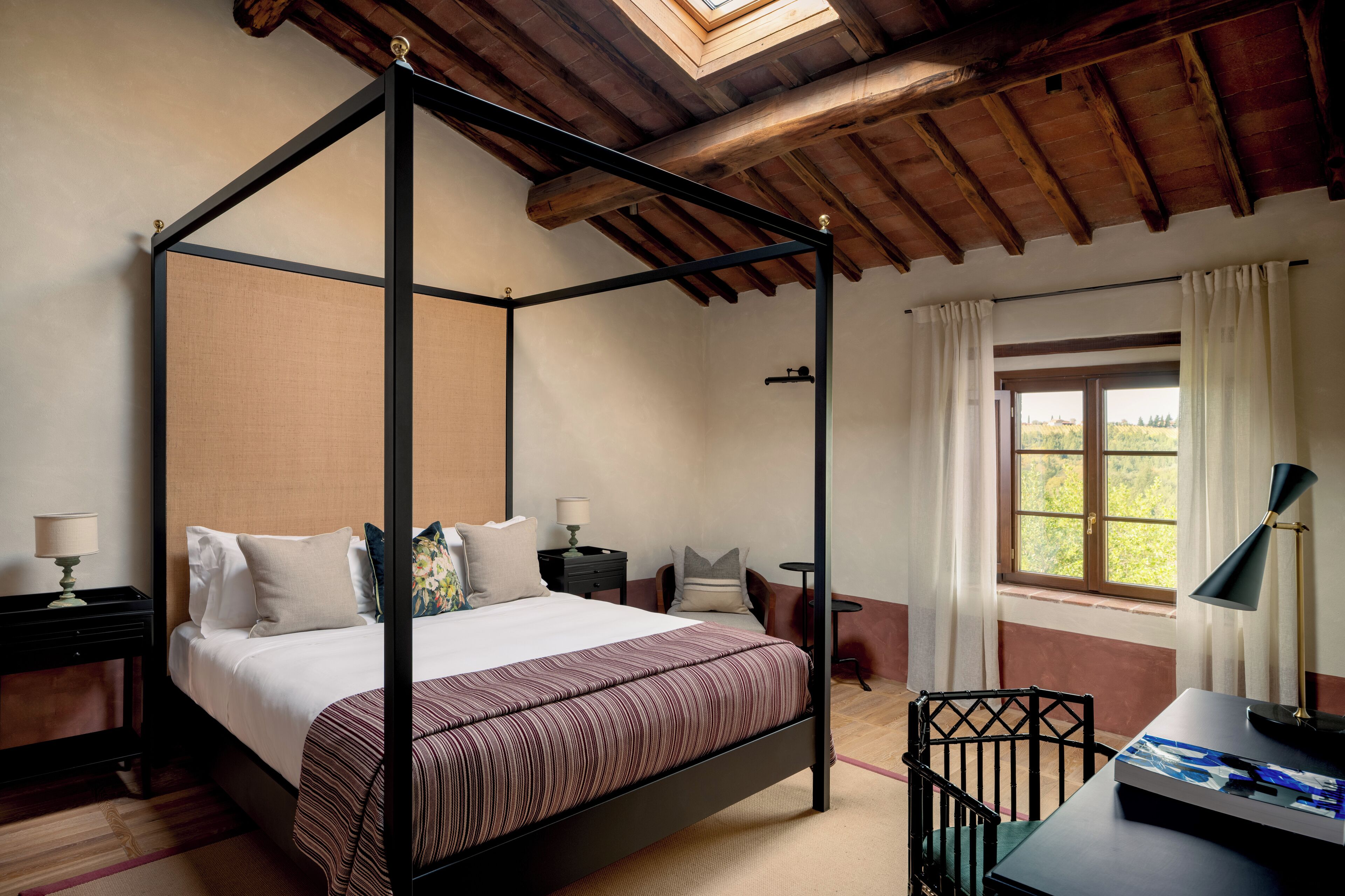A four-poster bed with a striped bedspread, a desk with a lamp, and a window with curtains.