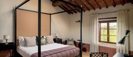 A four-poster bed with a striped bedspread, a desk with a lamp, and a window with curtains.