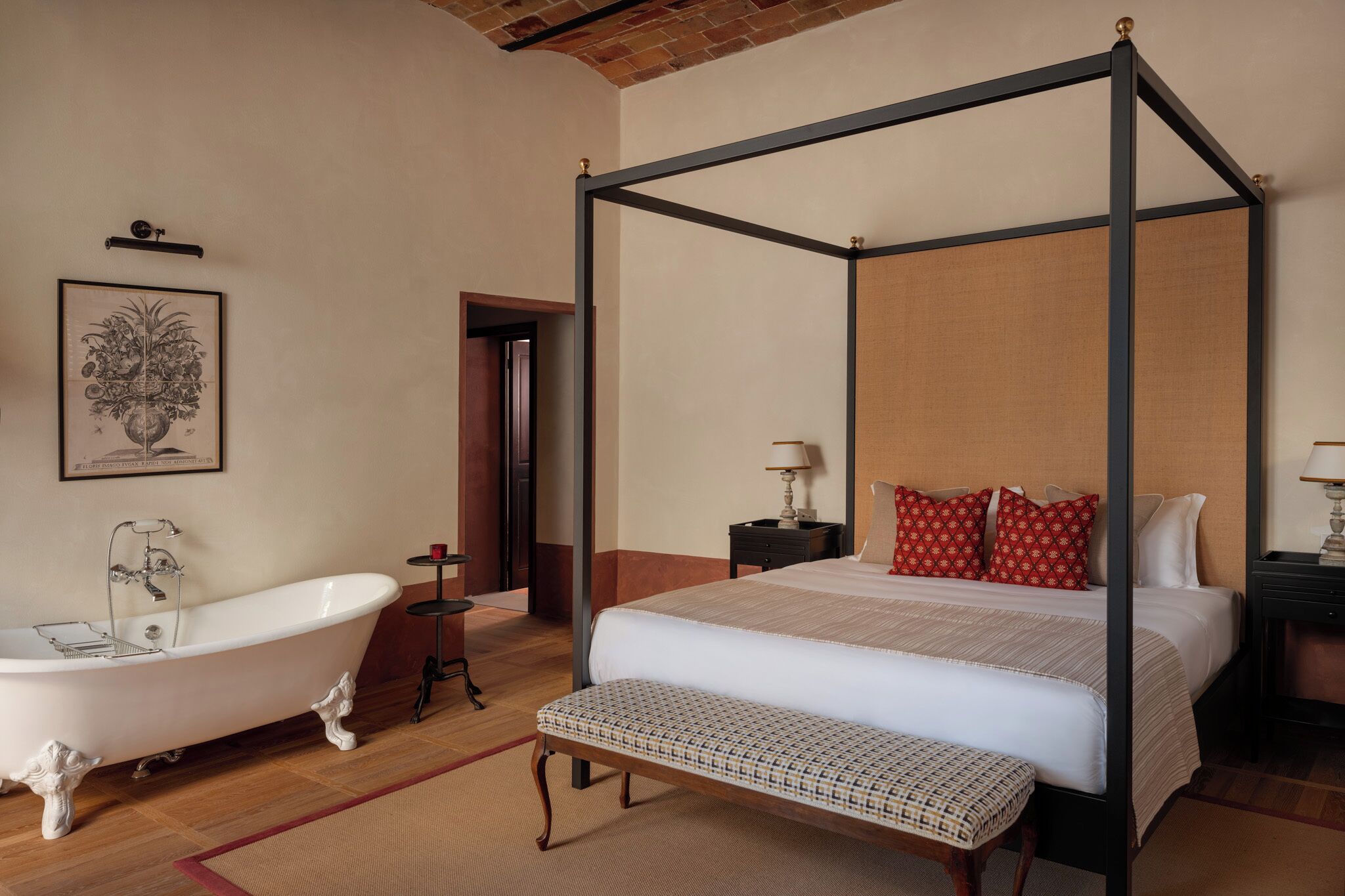 A four-poster bed with a wooden bench, a clawfoot bathtub, and a bedside table with a lamp.