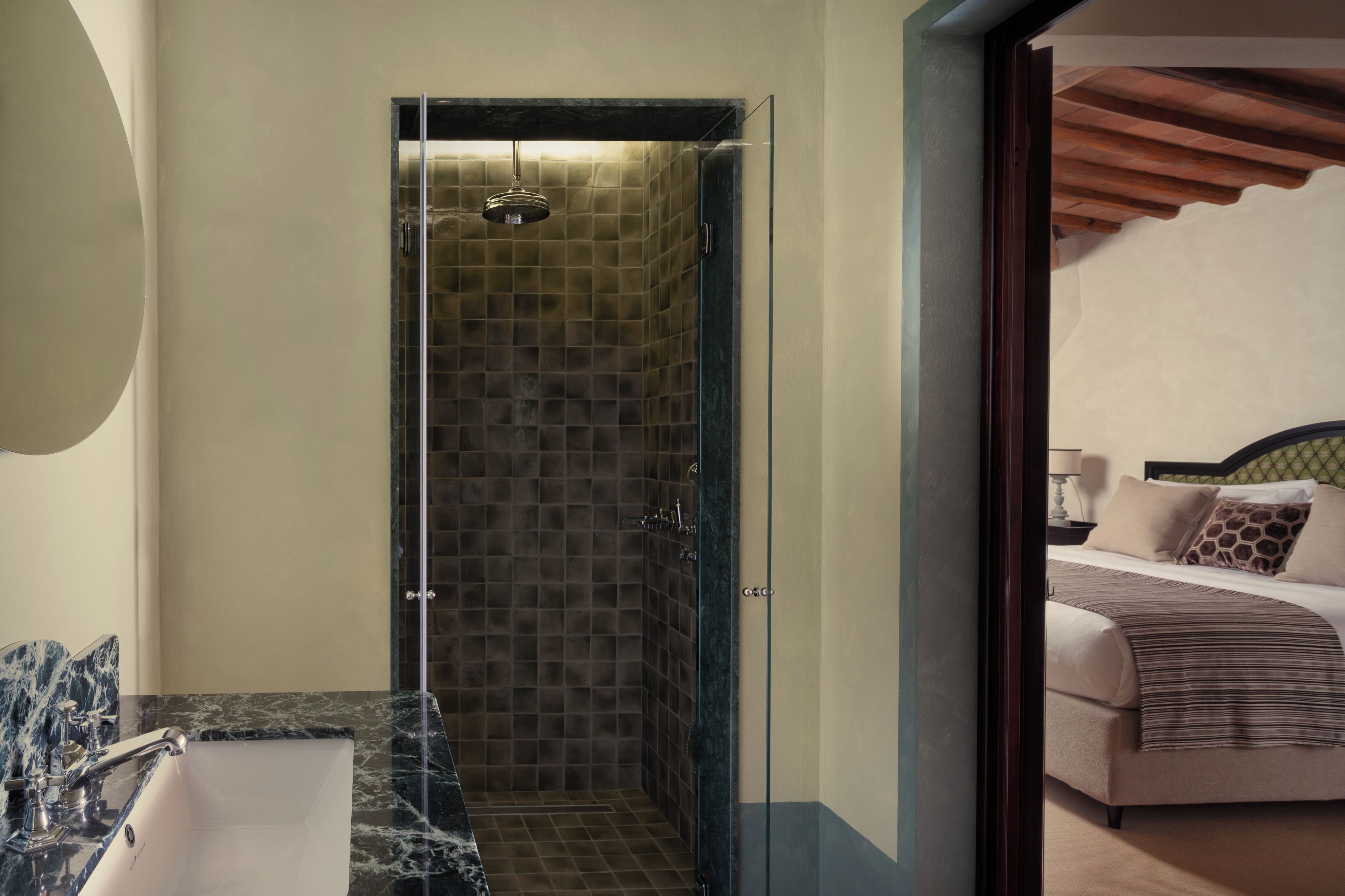 Un baño moderno con cabina de ducha de vidrio, lavamanos de mármol y, en la habitación contigua, una cama con cabecera de madera.