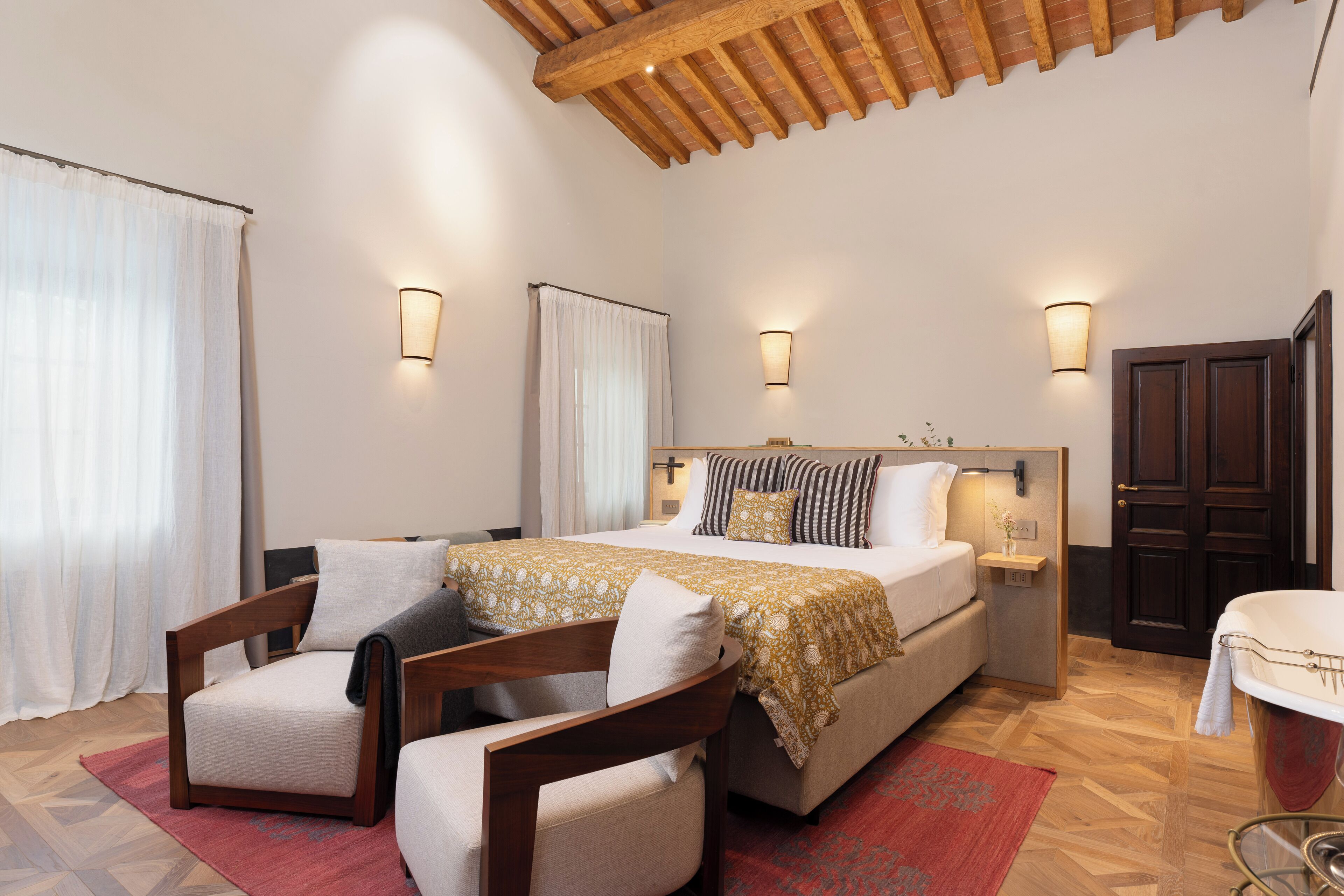 Un dormitorio con una cama grande, dos sillas, techo de madera y un baño con bañera.