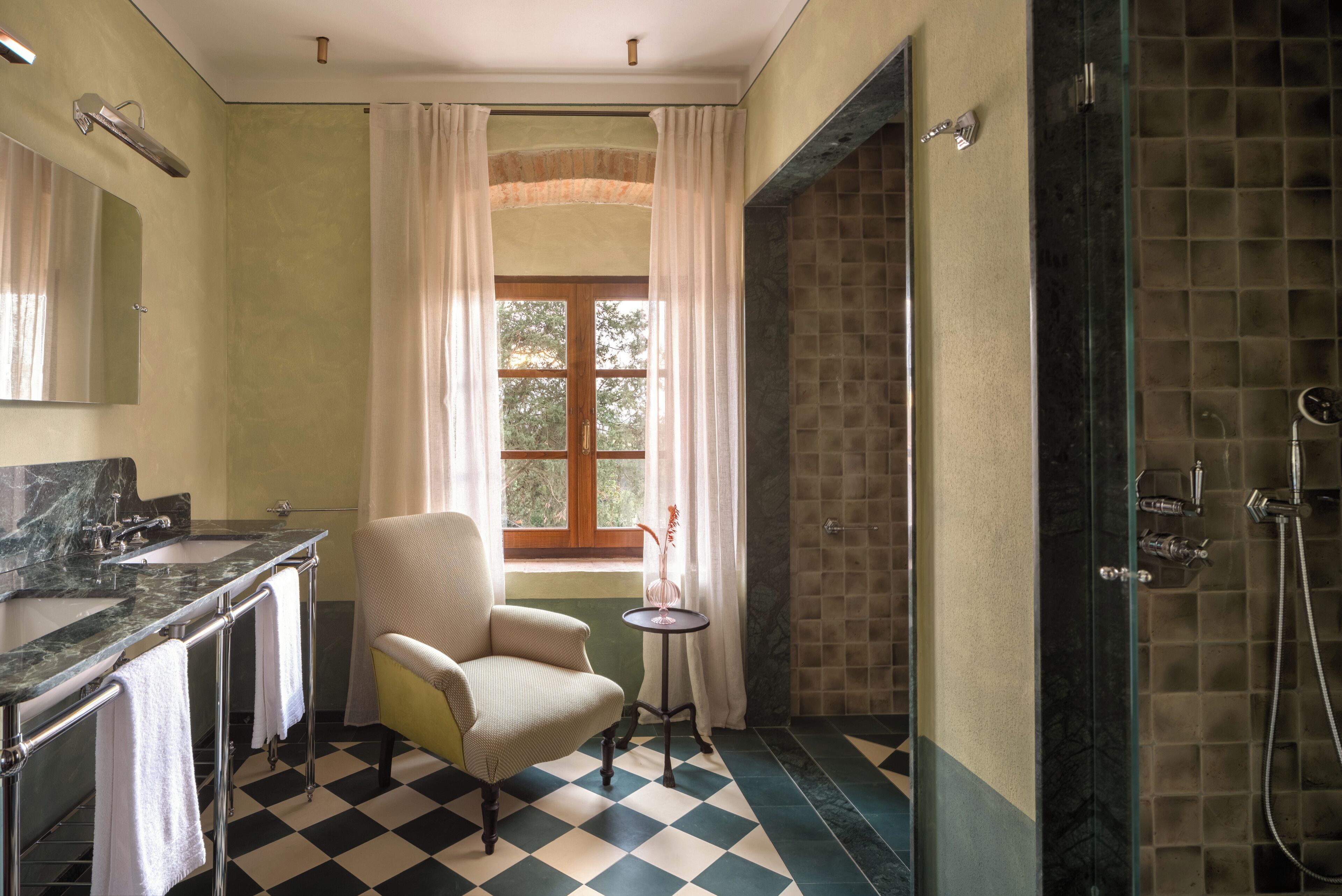 Baño con piso a cuadros, bañera, ducha, lavamanos y una silla.