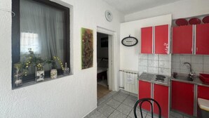 A compact kitchen with red cabinets, a window with a curtain, and a small dining area.