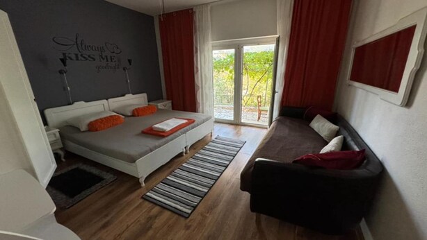A bedroom with a bed, a sofa, a window with curtains, a ceiling fan, and a wall with a motivational quote.