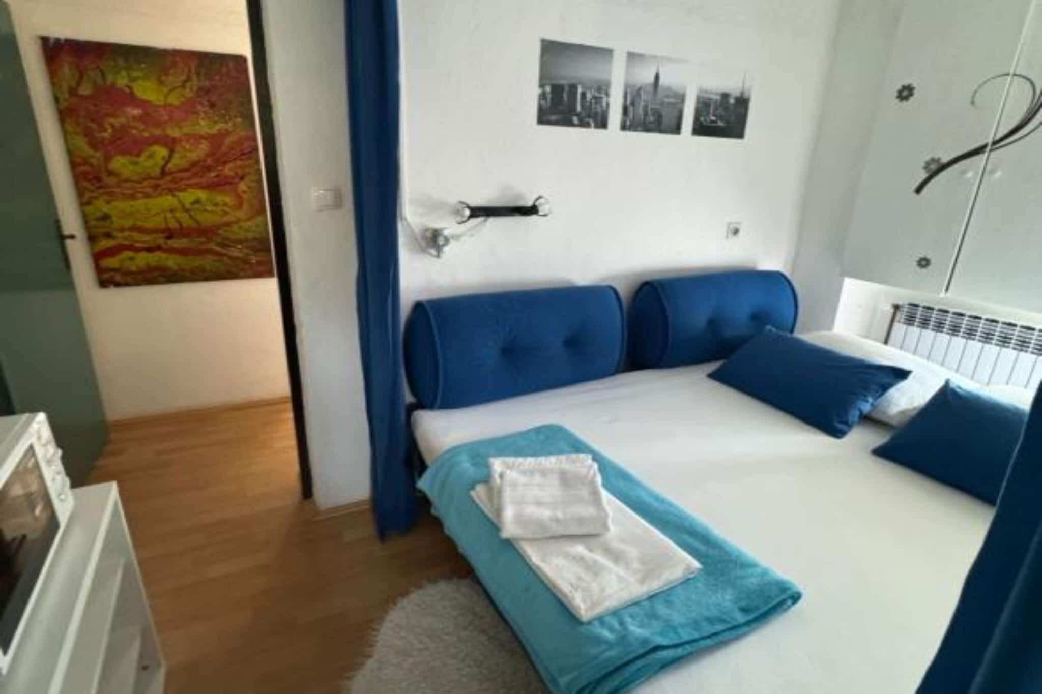 Une chambre à coucher avec un lit, une tête de lit bleue, du linge de lit blanc, une serviette bleue et un tableau accroché au mur.