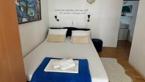 A neatly made bed with a blue blanket and two pillows, a wall with a motivational quote, and a small kitchenette in the background. - Duga House Apartment A3 (Crikvenica)