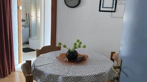 A round dining table with a patterned tablecloth, a vase with green plants, and a clock on the wall.