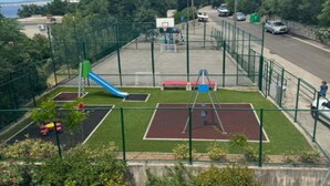 A fenced outdoor area with a basketball court, a slide, and a swing set.
