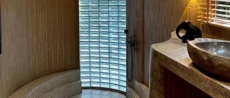 Une salle de bain moderne avec une douche aux lignes courbes, un grand miroir et un lavabo en pierre.