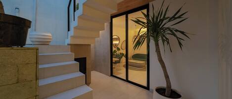 A modern interior with a staircase, a large potted plant, and a glass door leading to a seating area.