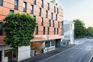 Un edificio a più piani con un ingresso sul cortile, una facciata in mattoni e un albero verde davanti.