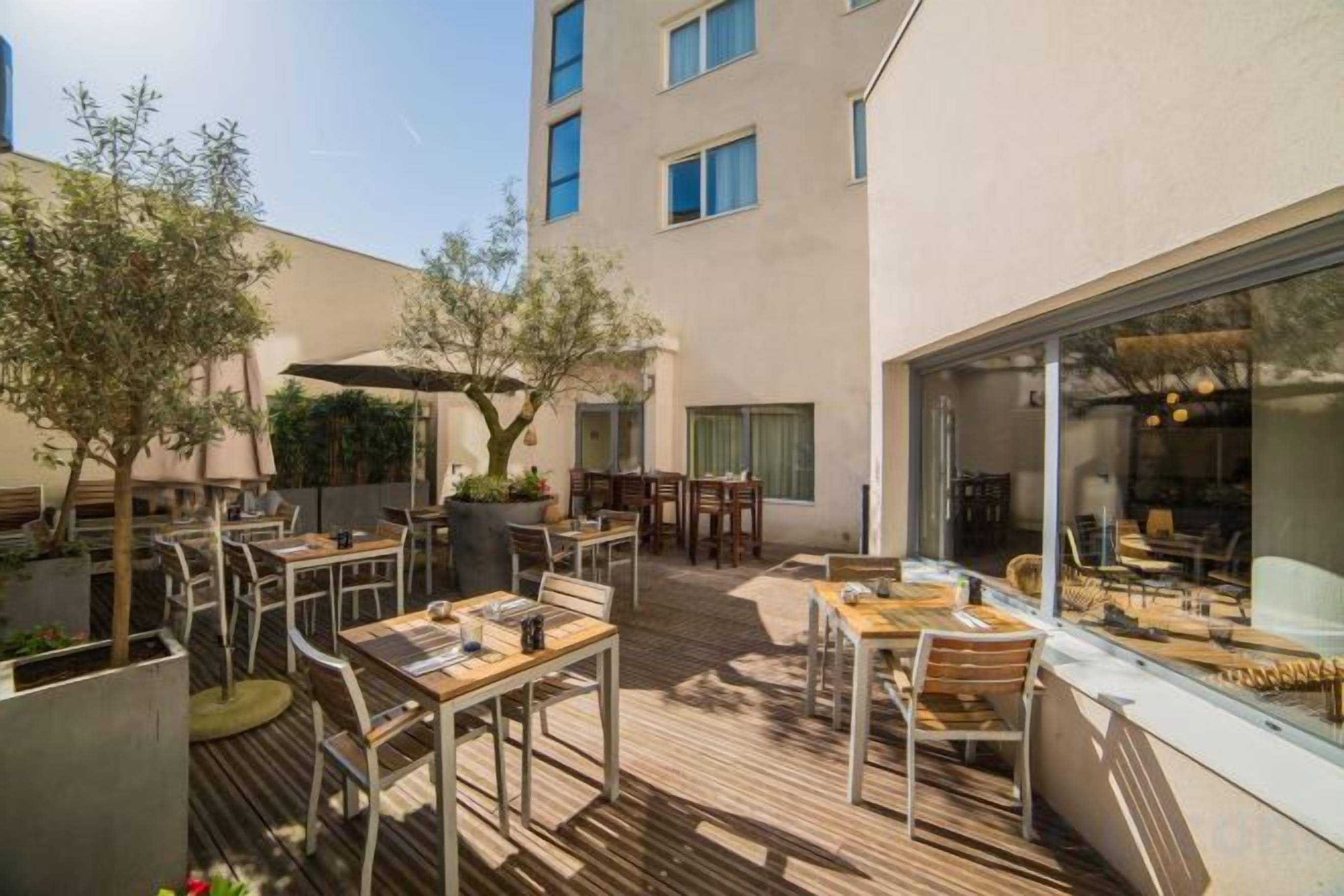 An outdoor patio with tables and chairs, a pergola, and a building with large windows.