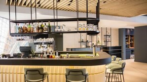 A modern bar area with a curved counter, bar stools, and shelves with bottles and glasses. - Courtyard Paris Arcueil (Arcueil)
