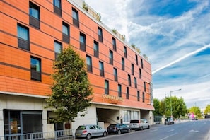 A multi-story hotel with a red facade, a tree in front, and parked cars along the street. - Courtyard Paris Arcueil (Arcueil)