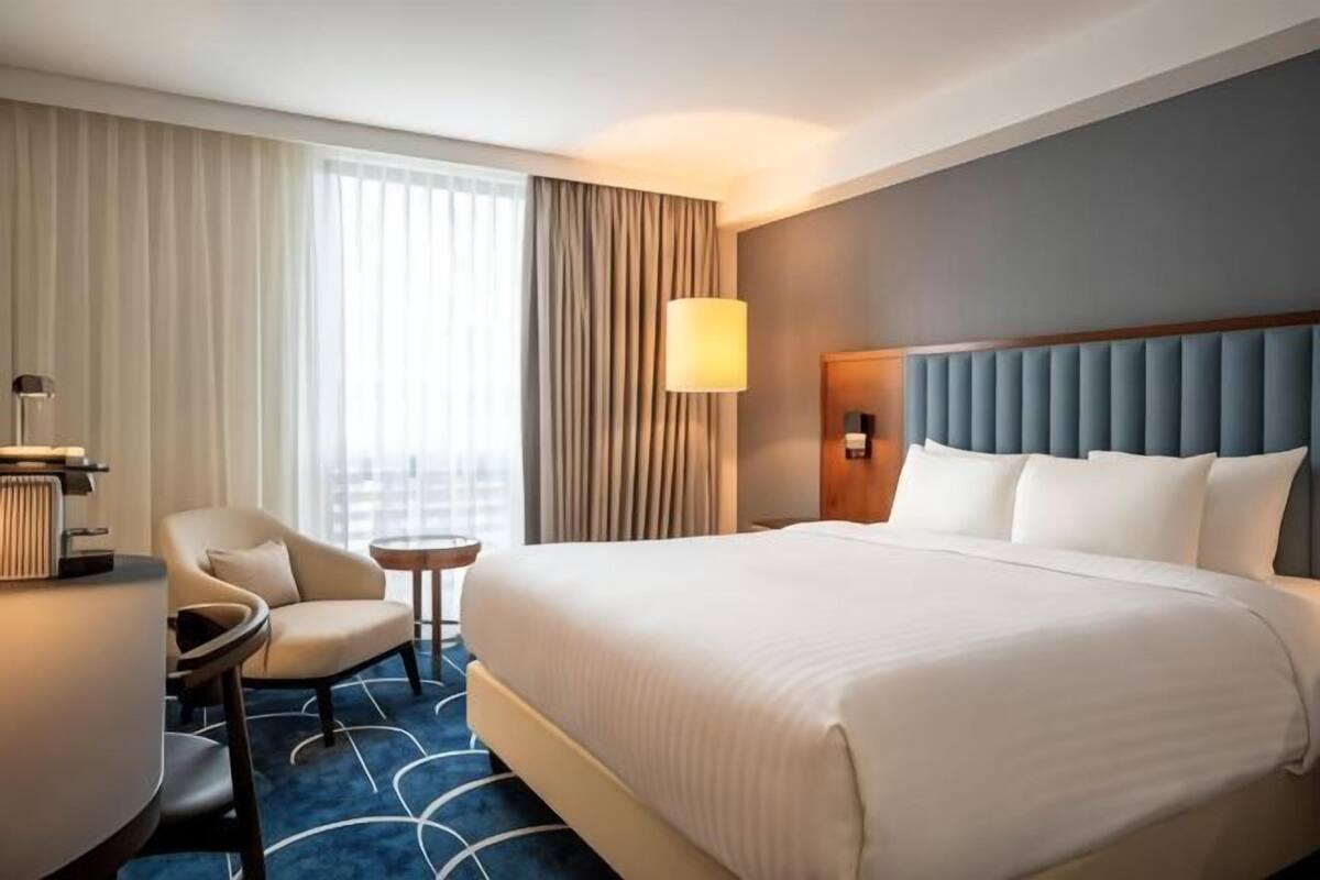 A hotel room with a large bed, a chair, a small table, and a lamp.