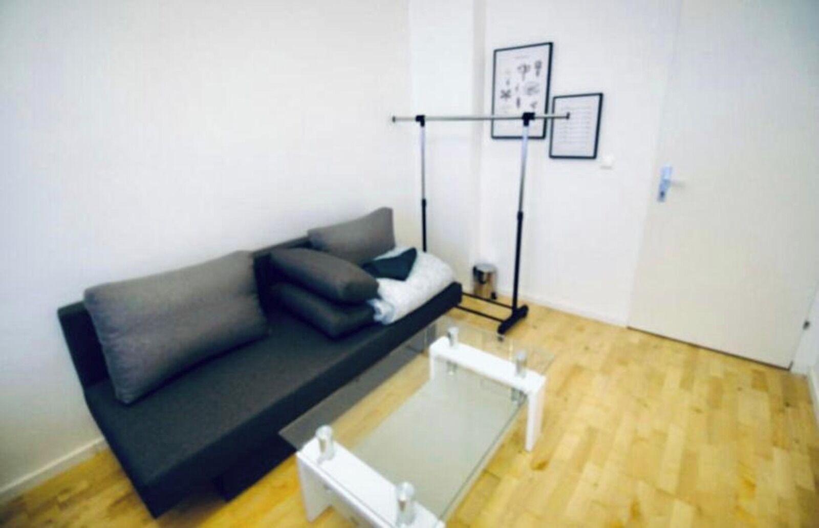 A modern living room with a dark grey sofa, a glass coffee table, and a wall-mounted TV.
