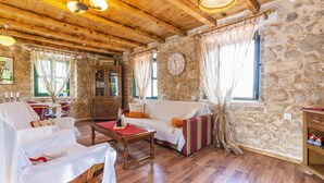 Una habitación acogedora con techo de madera, paredes de piedra, una mesa de madera, un sofá y un reloj en la pared.