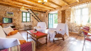 Una habitación acogedora con techo de madera, paredes de piedra, una escalera, un televisor y un comedor con mesa y sillas.