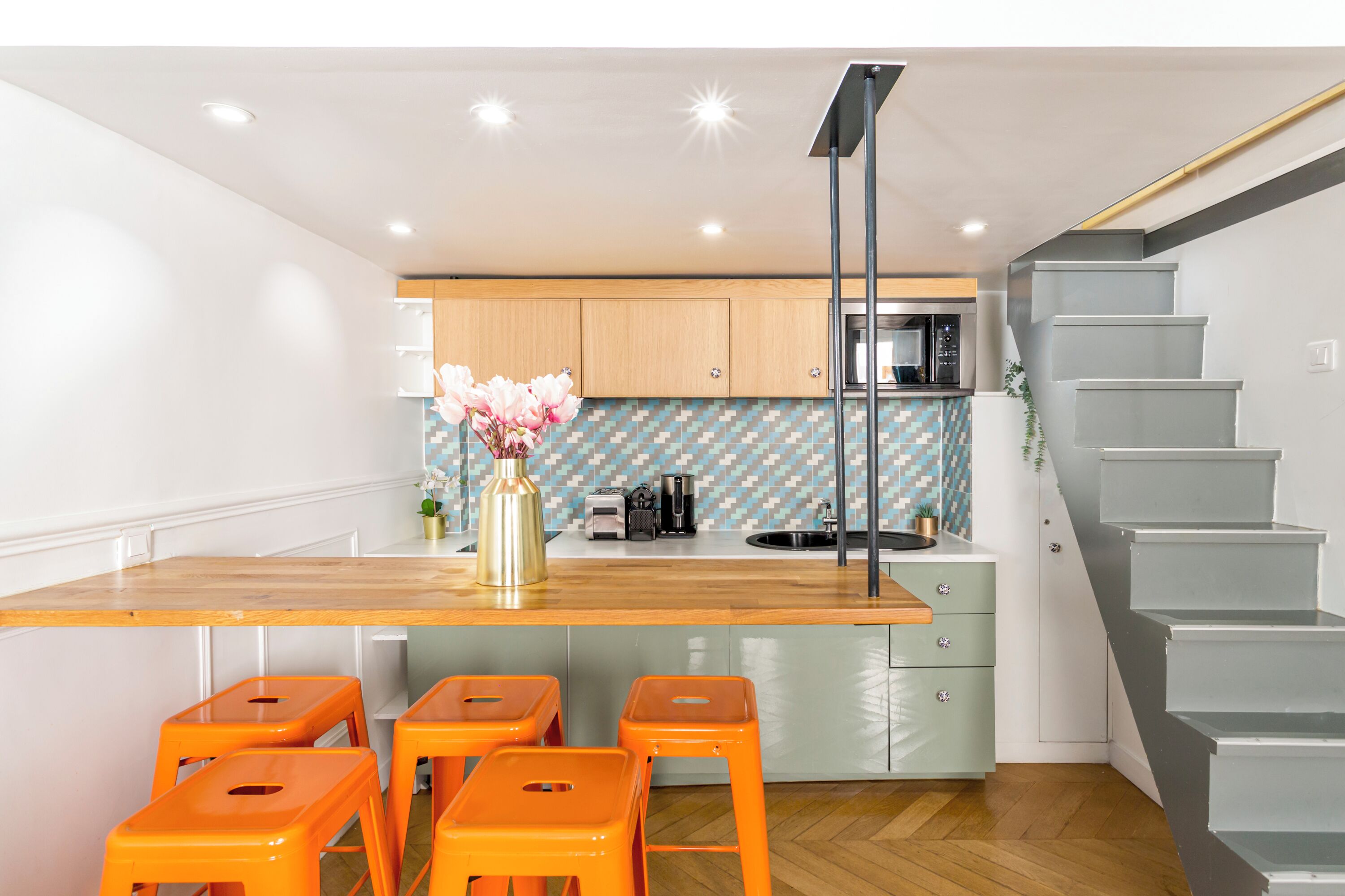 A modern kitchen with wooden countertops, a central island with bar stools, a microwave, and a patterned backsplash.