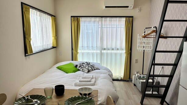 A modern hotel room with a bed, a dining table with plates and cups, and a ladder against the wall. - Corpo SKR (Musashino)