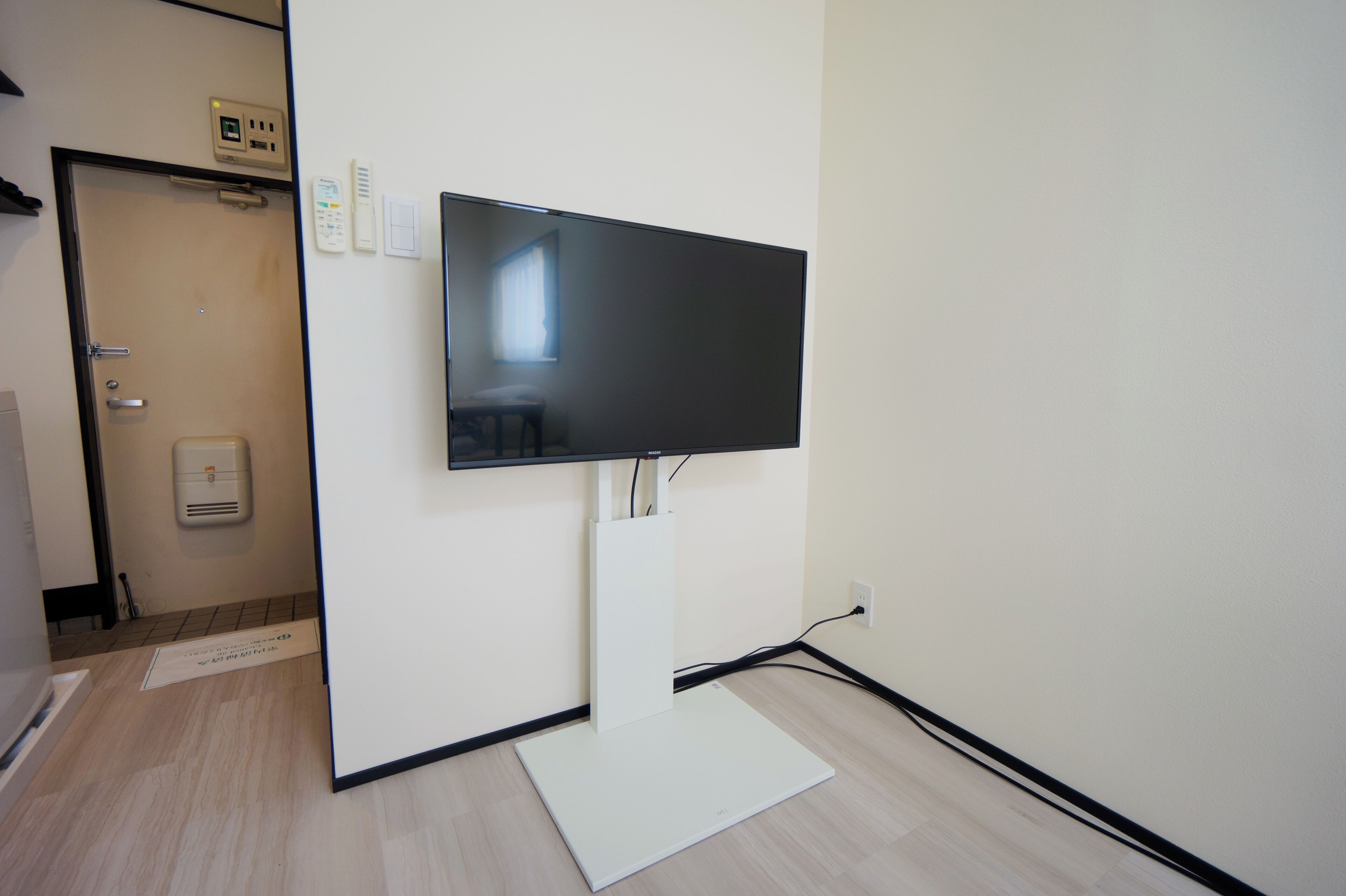 A flat-screen TV mounted on a wall in a room with a door, a thermostat, and a power outlet.