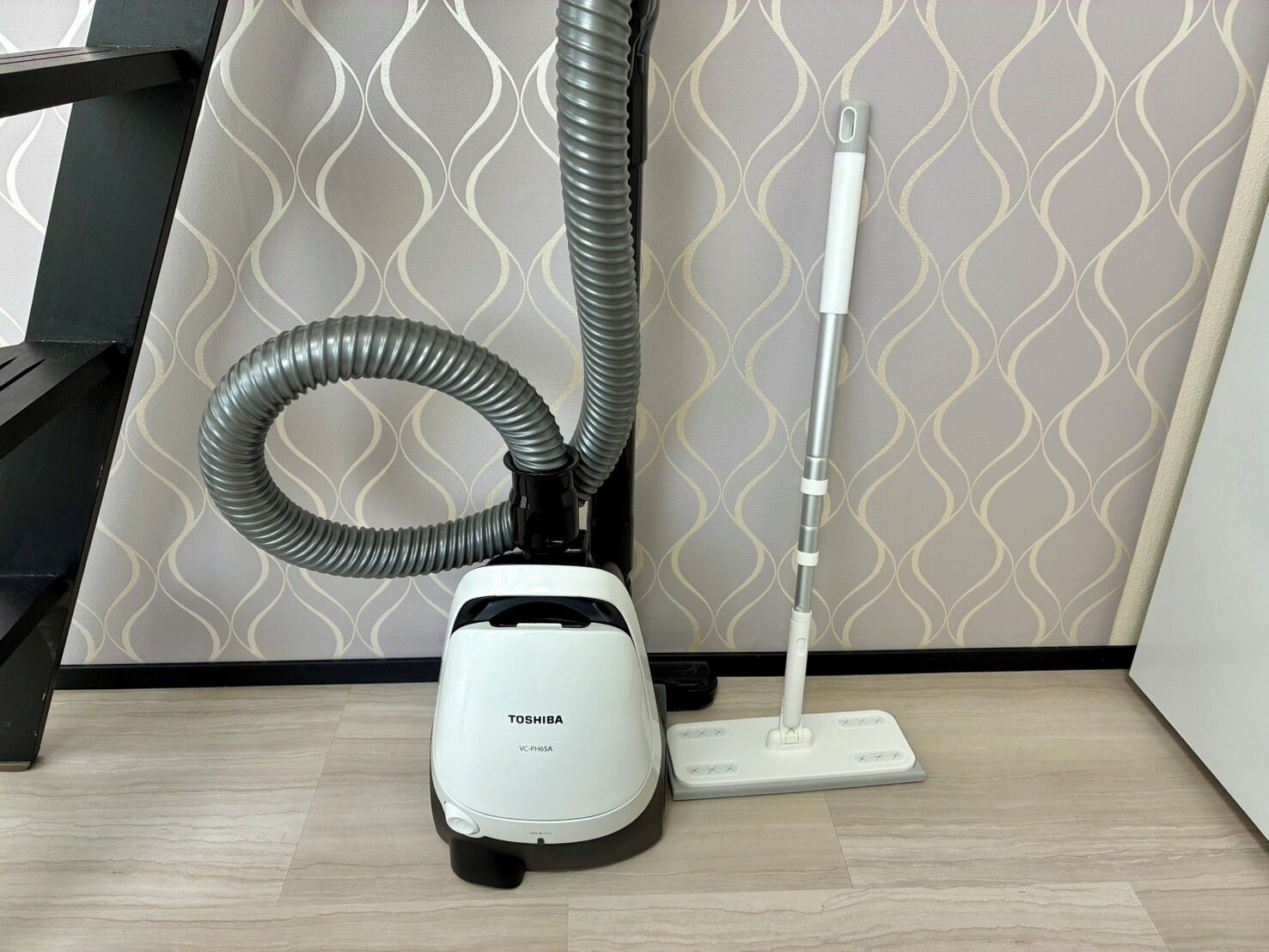 Aspiradora Toshiba con manguera y accesorio para fregar sobre un piso de madera.