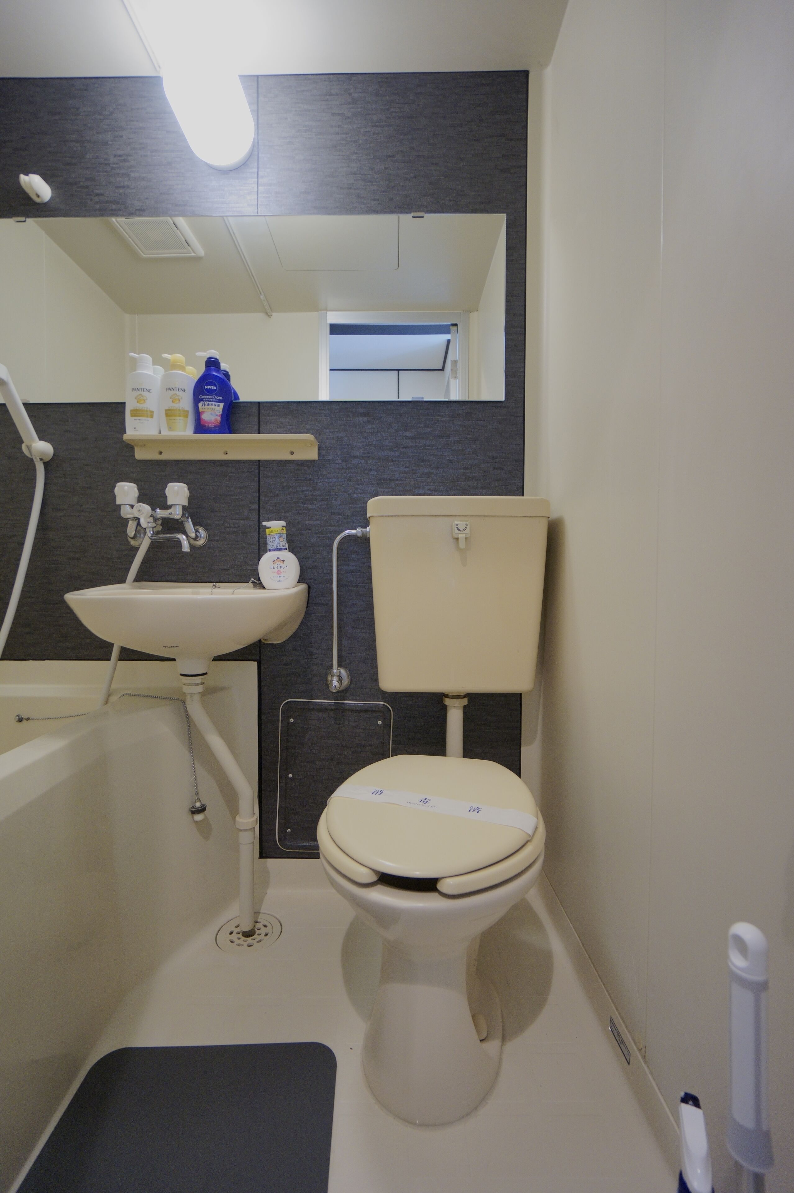 A compact bathroom with a white sink, toilet, and bathtub. A mirror hangs above the sink, and there are toiletries on a shelf.