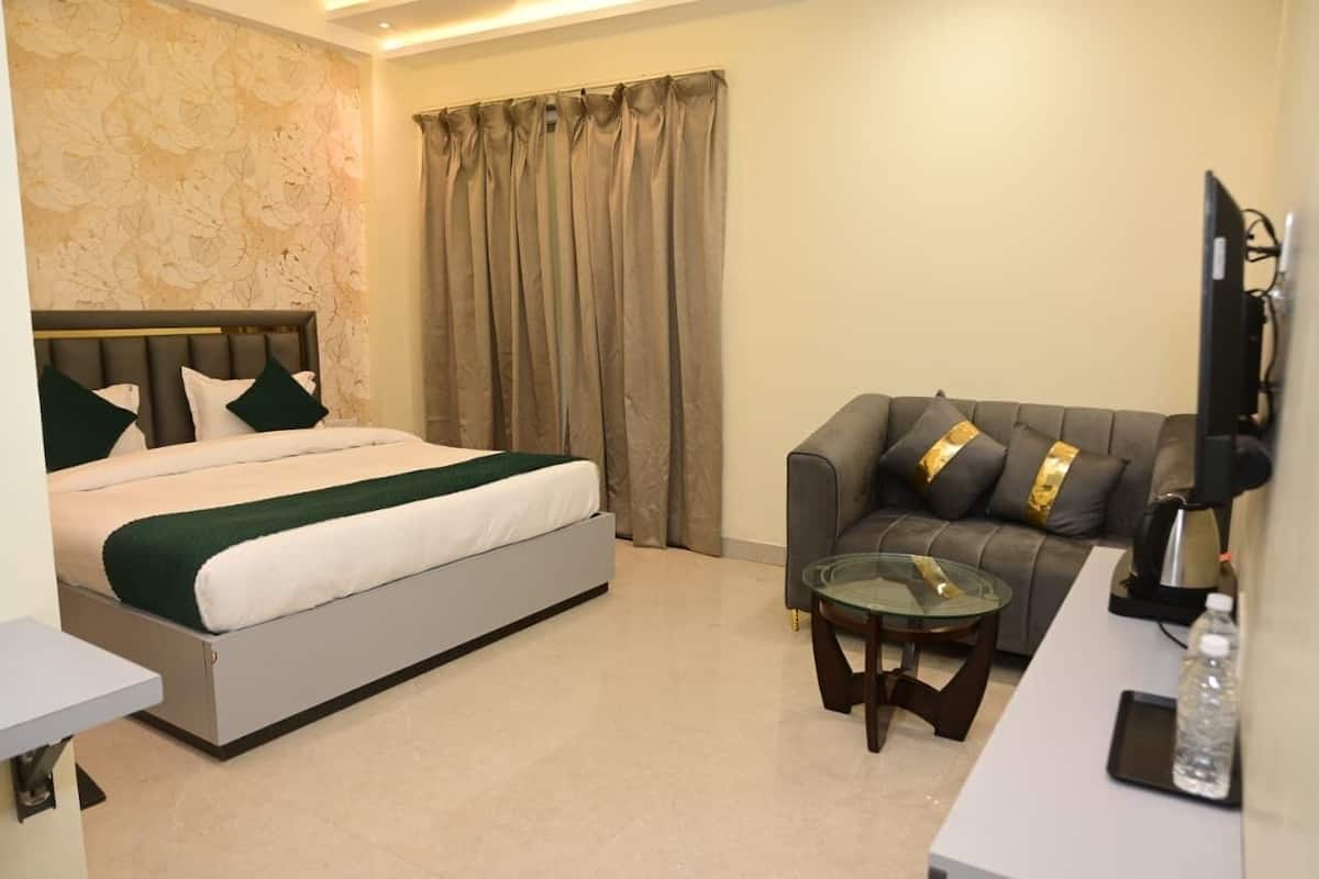 A hotel room with a bed, a sofa, a glass table, a TV, and a curtain.