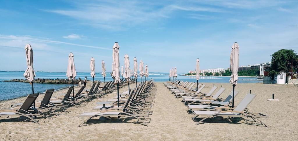Une plage bordée de rangées de chaises longues et de parasols, un ciel dégagé et une mer calme.