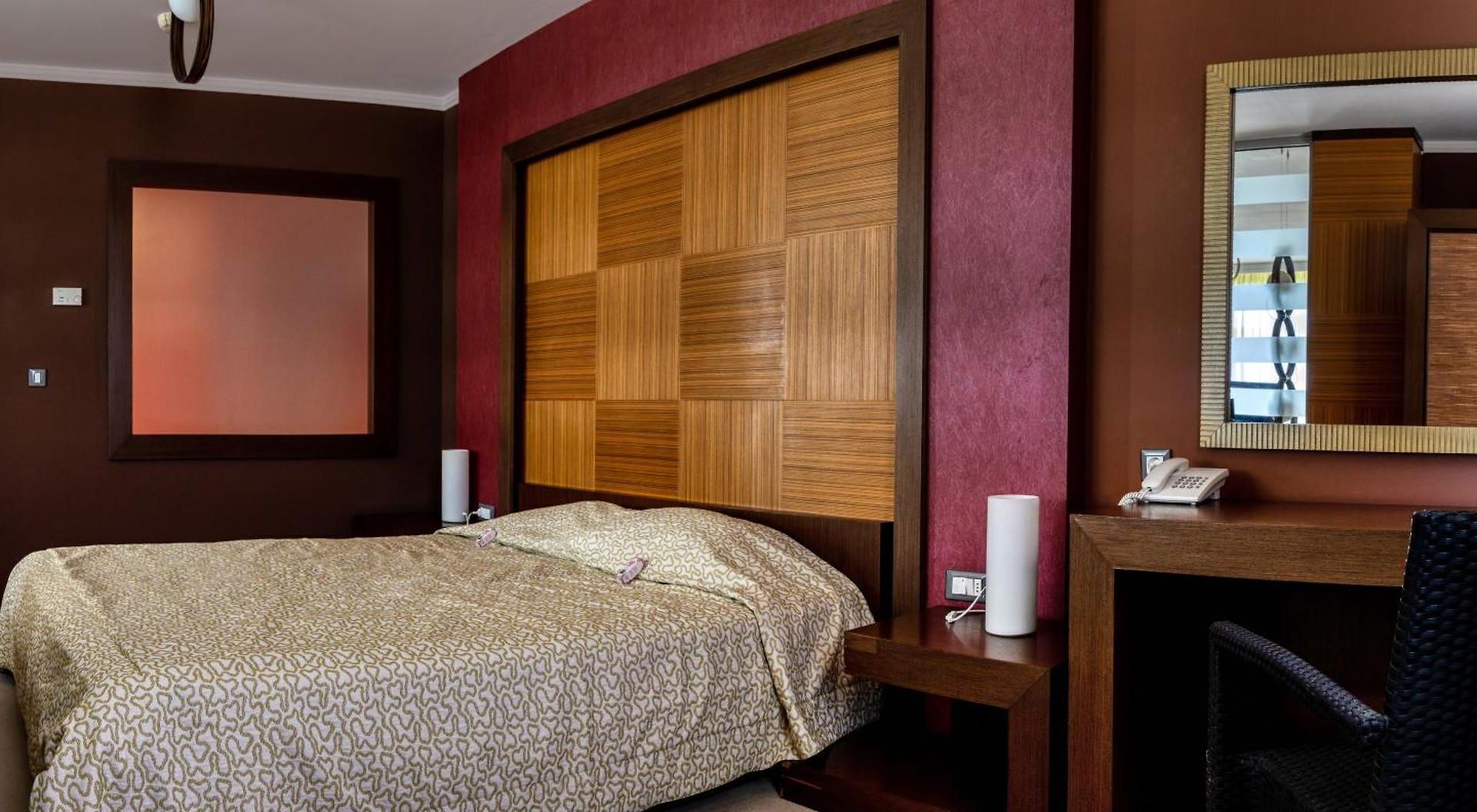 Habitación de hotel con cama, cabecera de madera, escritorio y teléfono, y un espejo.