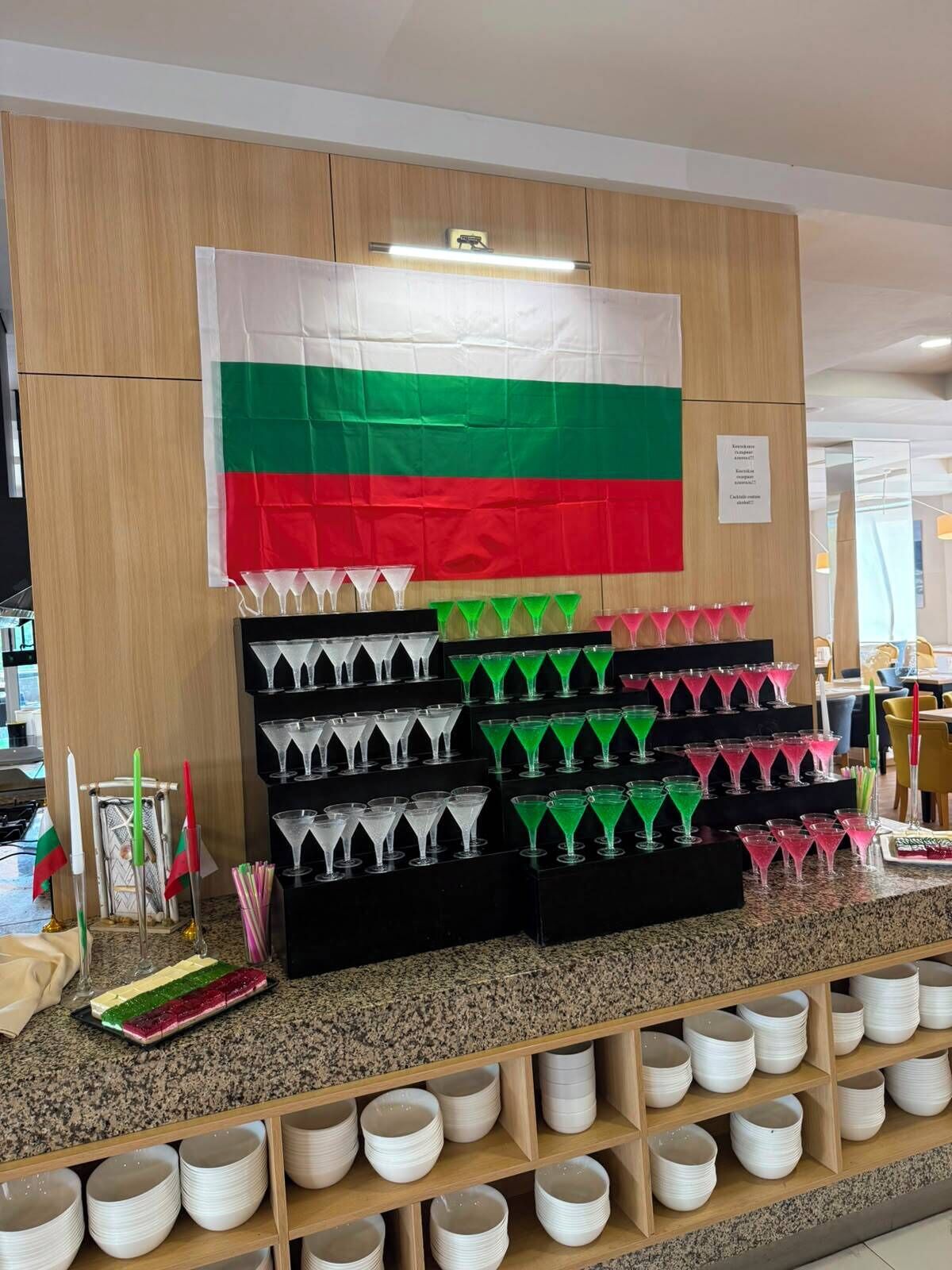 A display of martini glasses and cocktail shakers on a counter, with a flag and a sign in the background.