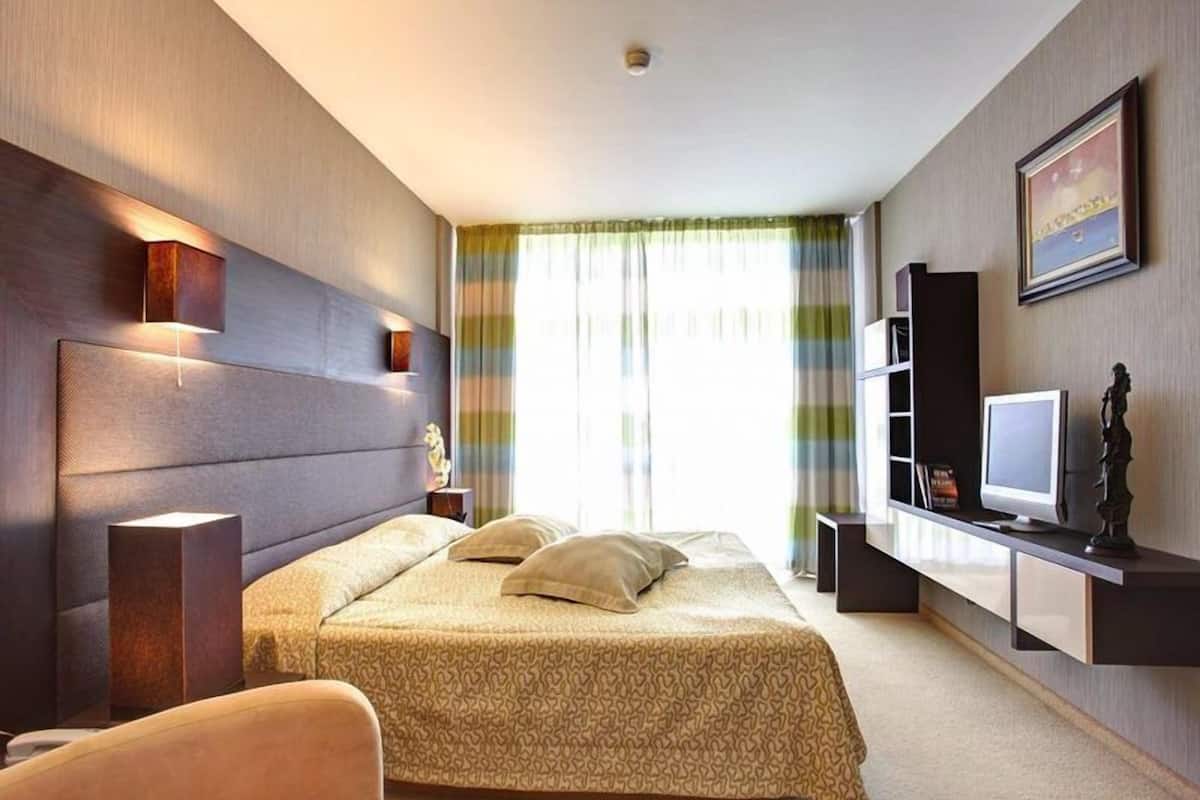 Ett modernt hotellrum med en stor säng, ett skrivbord med en dator och en bokhylla.