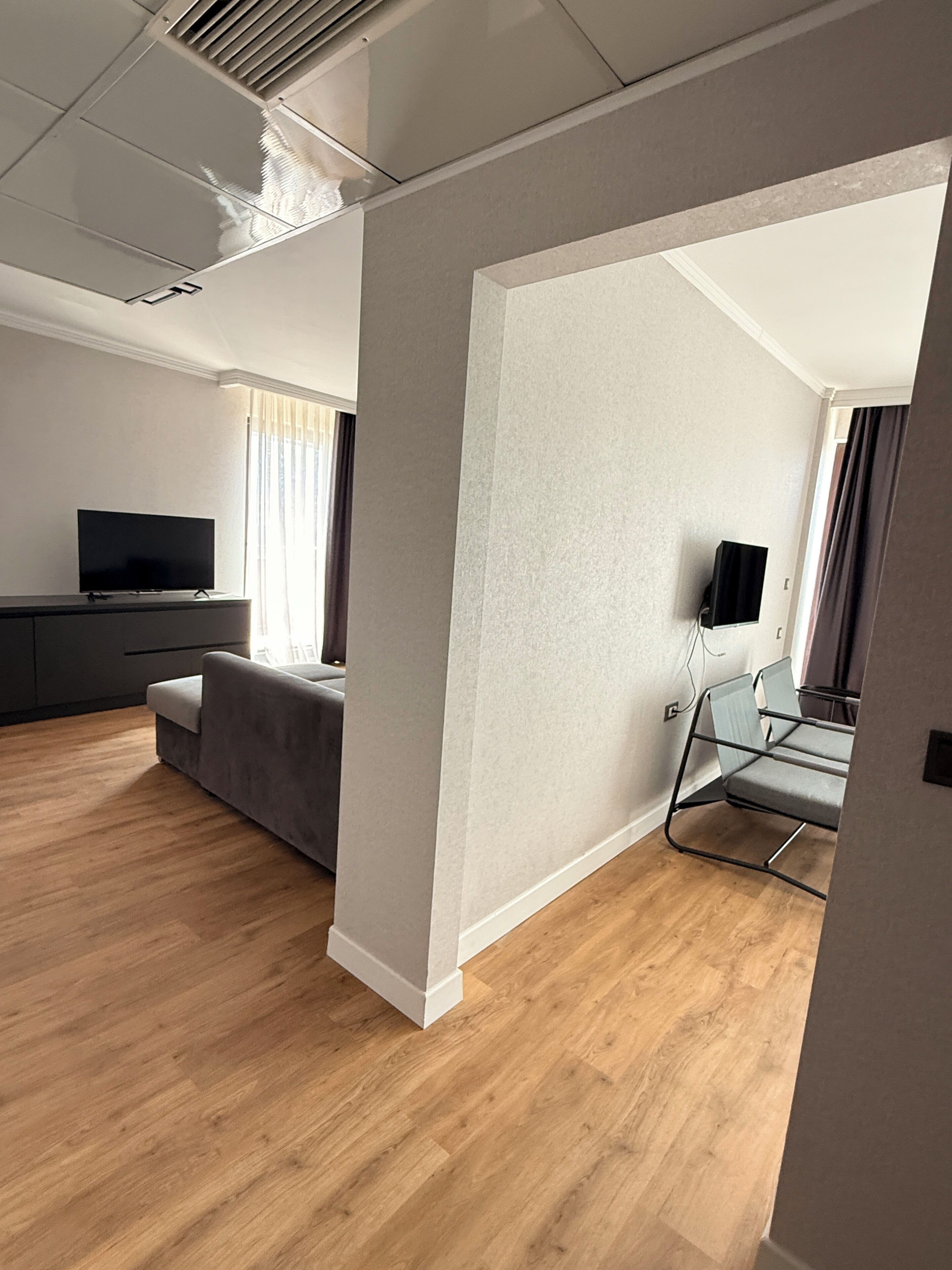A modern living room with a flat-screen TV, grey sofa, and a glass table.