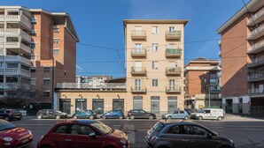 A multi-story residential building with balconies, a ground-level commercial area with shops, and parked cars on the street. - Casa Maha by Wonderful Italy (Turin)