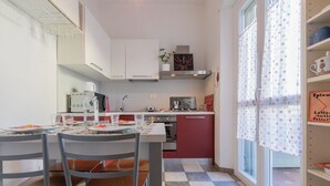 A modern kitchen with white cabinets, a red countertop, and a checkered floor. There is a dining table with chairs and a window with curtains. - Casa Maha by Wonderful Italy (Turin)