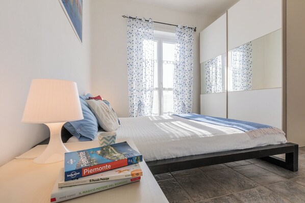 A bedroom with a bed, a bedside table with a lamp, and a window with curtains.