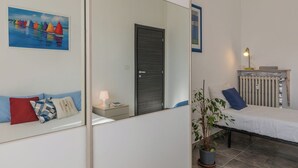A bedroom with a bed, a nightstand, a lamp, a radiator, a plant, and a painting of sailboats on the wall. - Casa Maha by Wonderful Italy (Turin)