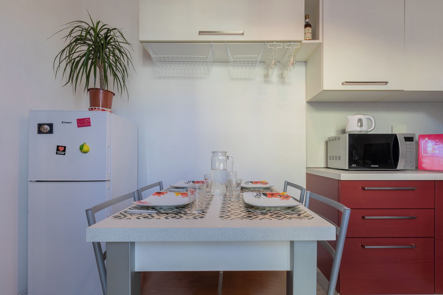 Een kleine keuken met een koelkast, magnetron en een eettafel voor twee personen gedekt.