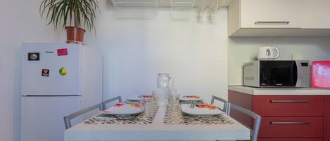 Een kleine keuken met een koelkast, magnetron en een eettafel voor twee personen gedekt.