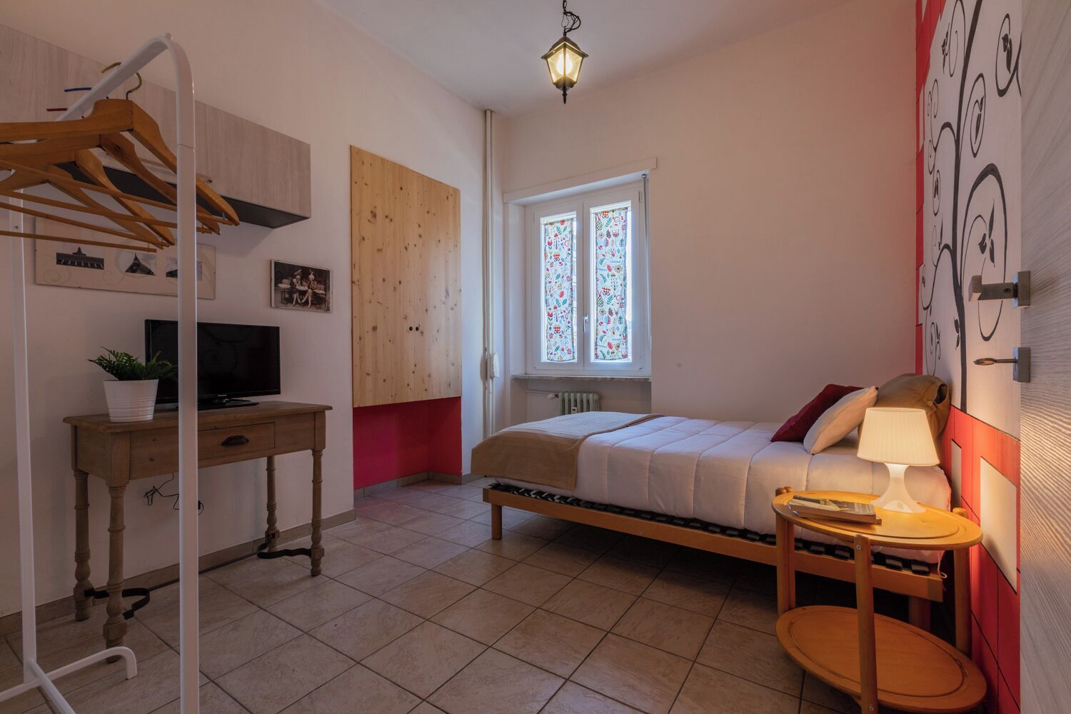 Une chambre à coucher comprenant un lit, une table de chevet, une lampe et un bureau avec une télévision et une plante.