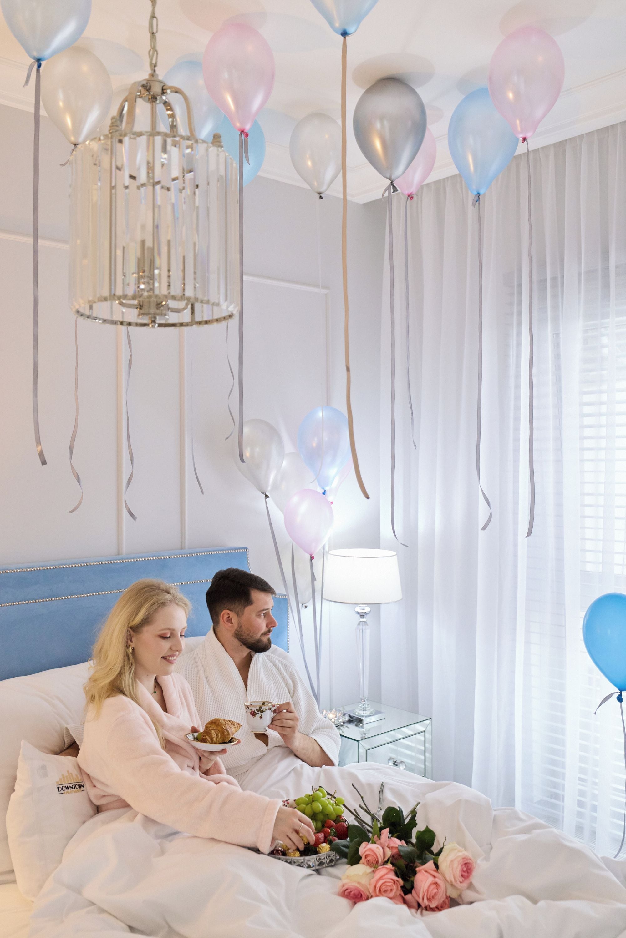 A room with a bed, a bedside table with a lamp, and balloons.