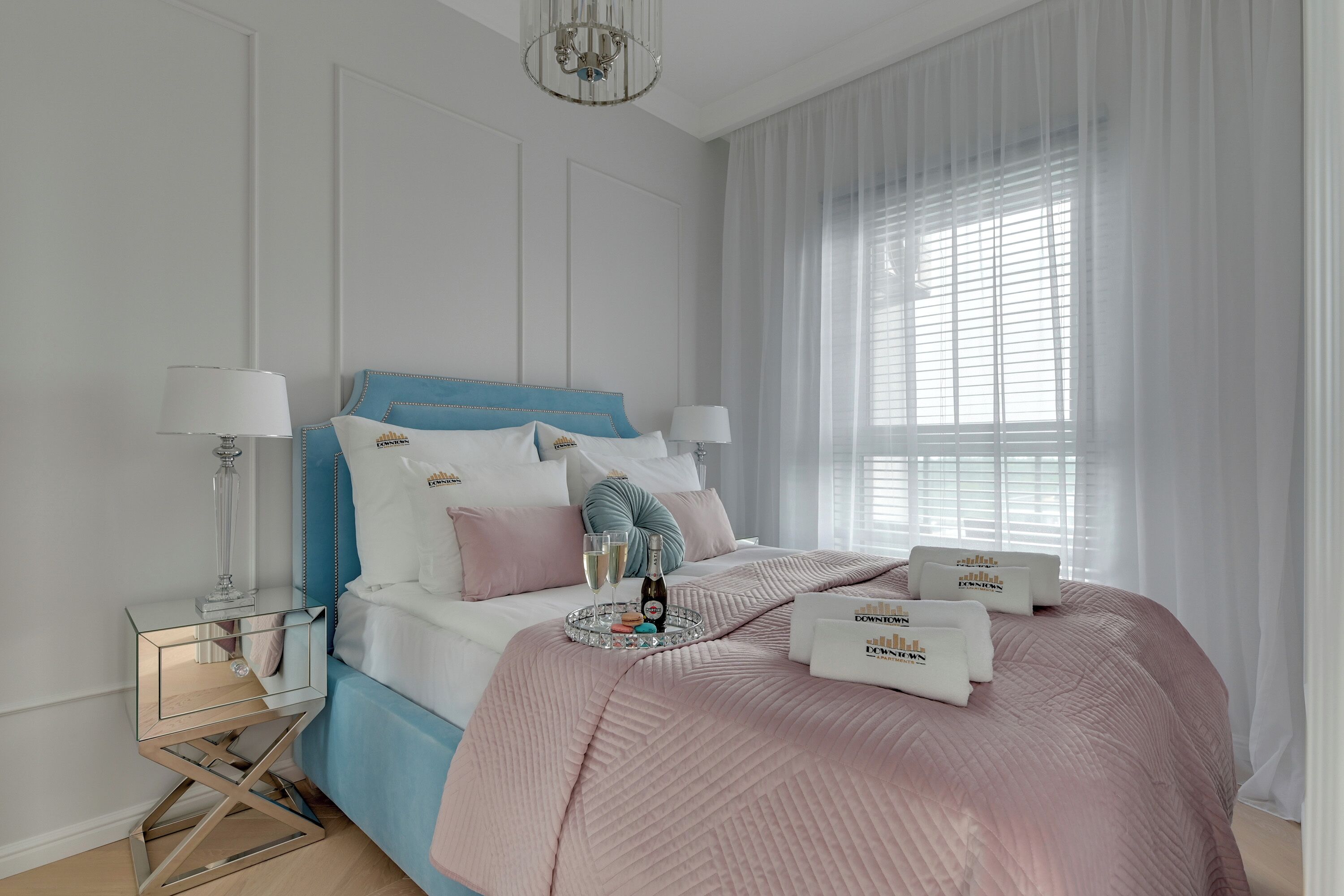 A neatly arranged bedroom with a bed, bedside tables, and a window with sheer curtains.