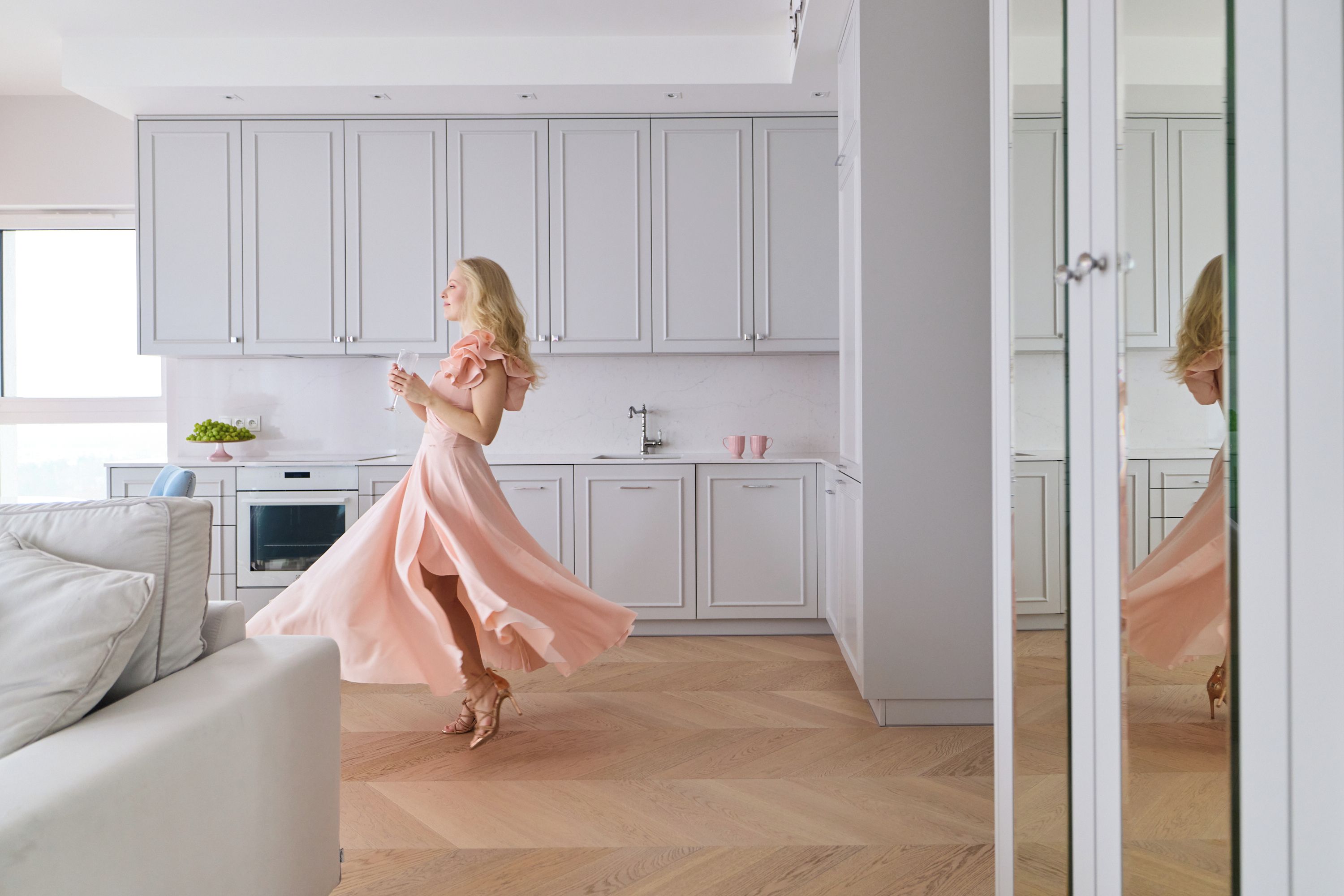 A modern kitchen with white cabinets, a dining area with a white sofa, and a large mirror reflecting the room.