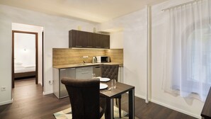 A compact kitchen with dark wooden cabinets, a microwave, and a dining area with a table and chairs. - Paulay Downtown Apartments (Budapest)