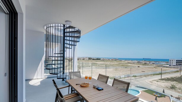 A balcony with a wooden table, chairs, and a spiral staircase.