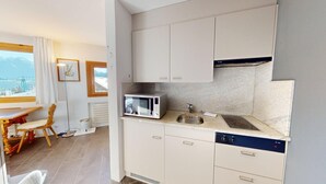 Een kleine keuken met een magnetron, spoelbak en vaatwasser. Er is een eethoek met een tafel en stoelen.