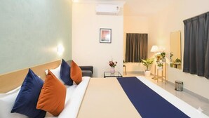 Habitación de hotel con cama, mesita de noche con lámpara, una pequeña mesa con un florero y una ventana con cortinas.