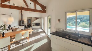 Une cuisine moderne dotée d’une grande fenêtre, un coin repas avec une table et des chaises en bois, et un espace de vie avec un canapé et un téléviseur.