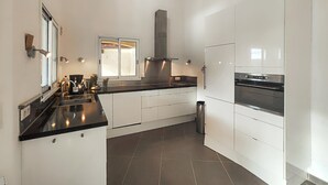 Une cuisine moderne avec des armoires blanches, une hotte en acier inoxydable, un four encastré et un plan de travail noir.